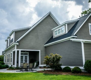 Gray two-story house with white trim, siding installations & repairs, a covered porch, and a manicured lawn.