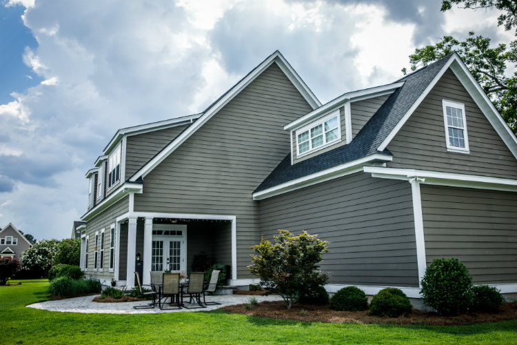 Gray two-story house with white trim, siding installations & repairs, a covered porch, and a manicured lawn.